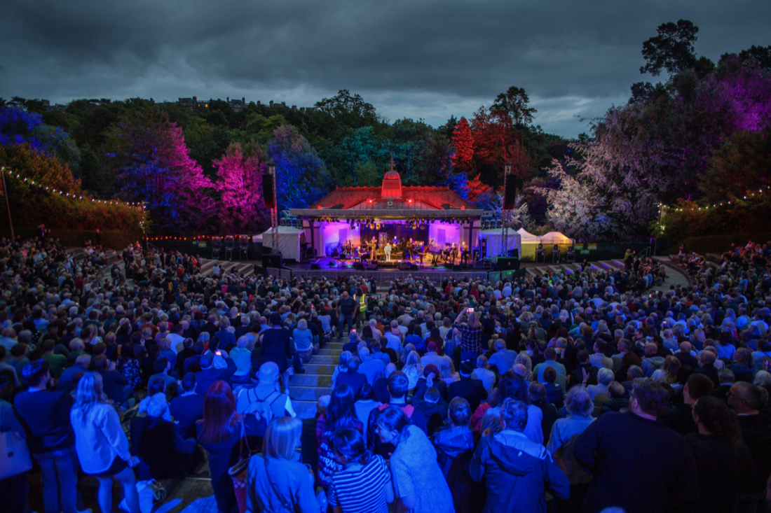 A packed Kelvingrove Bandstand at night with stage lights lighting up the trees.