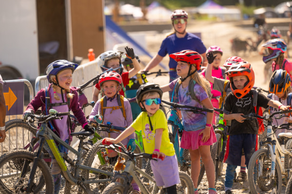 A group of kids stand around with their mountain bikes